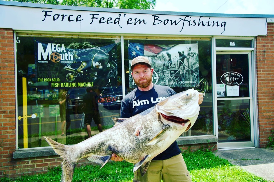 Capt. Justin Cook holding a large Asian carp outside Force Feed'em Bowfishing